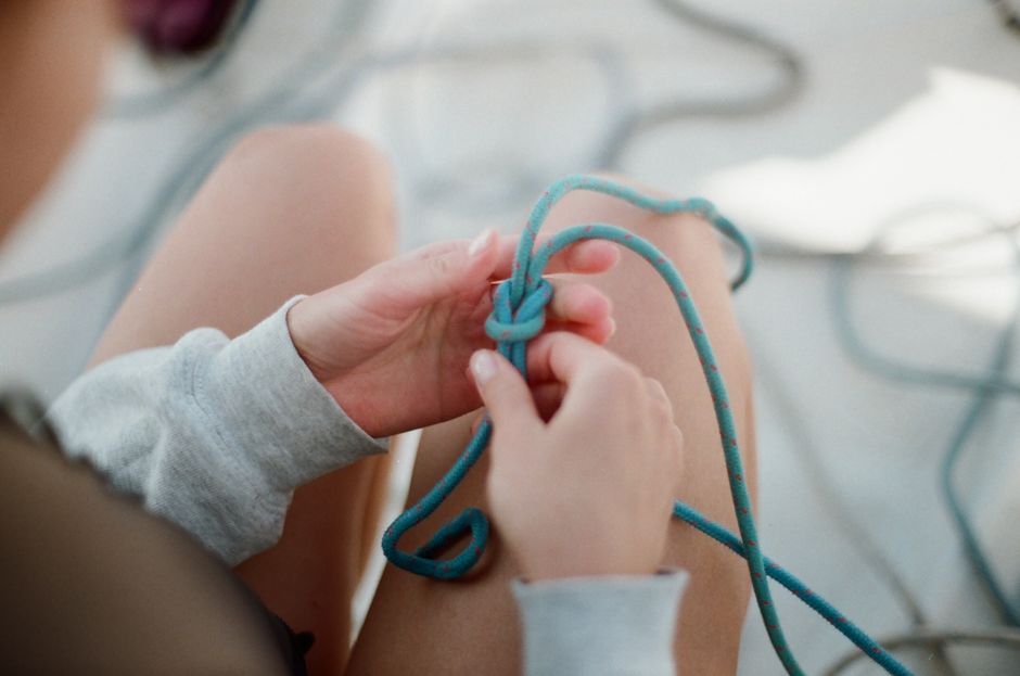 Detail shot of hands tying a blue rope knot, showcasing craftsmanship and technique.